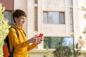 Teenage boy stands near a high-rise building, looking at his smartphone and smiling. Represents urban lifestyle, digital connection, and daily life in the city
