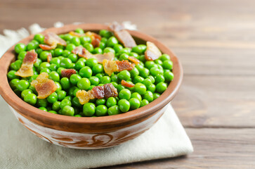 Boiled green peas with fried crispy bacon in a brown ceramic bowl on a wooden table. Concept of an old recipe. Simple dishes. Rustic style. Horizontal orientation. Selective focus. Copy space.
