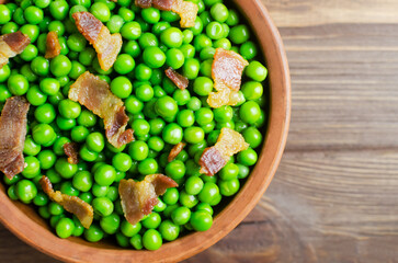 Boiled green peas with fried crispy bacon in a brown ceramic bowl on a wooden table. Old recipe concept. Simple dishes. Rustic style. Horizontal orientation. Selective focus. Copy space. Top view.
