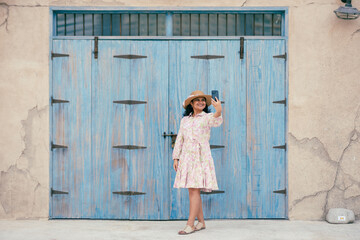 young woman in floral dress and hat clicking photos at Al seef historical neighborhood in Dubai,...