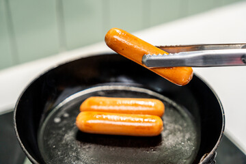 A hand expertly flips sausages in a hot pan sizzling as they cook. Sausages sizzle and brown in a pan a hand carefully turning them. Close-up of a hand frying sausages in a pan.