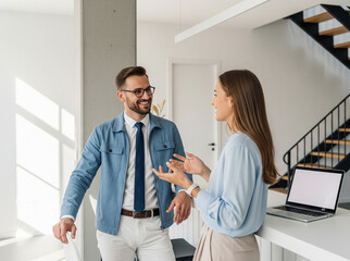 Fototapeta premium Two people are having a casual conversation in a minimalist workspace, reflecting a harmonious and enthusiastic working relationship.