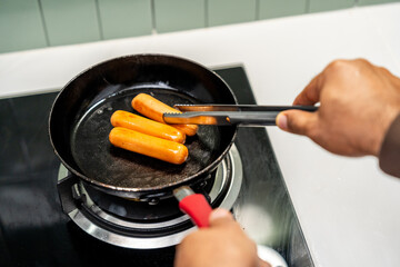 A hand expertly flips sausages in a hot pan sizzling as they cook. Sausages sizzle and brown in a pan a hand carefully turning them. Close-up of a hand frying sausages in a pan.