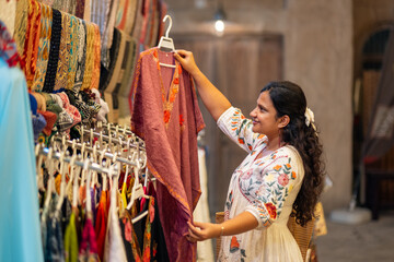 young Asian woman street shopping in Mumbai, she is looking at beautiful kaftan style dresses on...