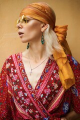 A stylish woman with a floral dress and yellow headscarf posing beautifully.
