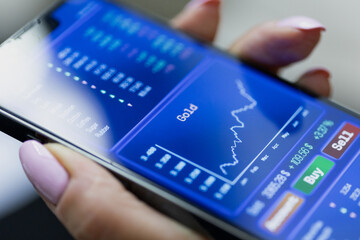 Woman holding smartphone with stock market information, prices and charts. Internet trading, brokerage, commodity information, investment, risk, success, business.