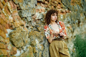 A stylish young woman in a floral shirt leans against a textured brick wall.