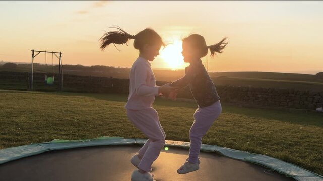 4K: Grils jumping on Trampoline at Sunset. Sisters having fun outdoors in the Garden in summer. Stock Video Clip Footage