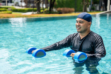 A smiling person in a swim cap and rash guard is submerged in a pool, holding blue aquatic...