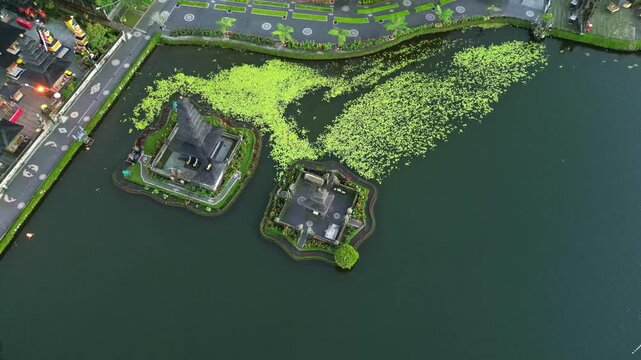 Aerial view of Ulun Danu Beratan temple on the lake, with bright green vegetation contrasting with the dark water, Candikuning, Kabupaten Tabanan, Indonesia.