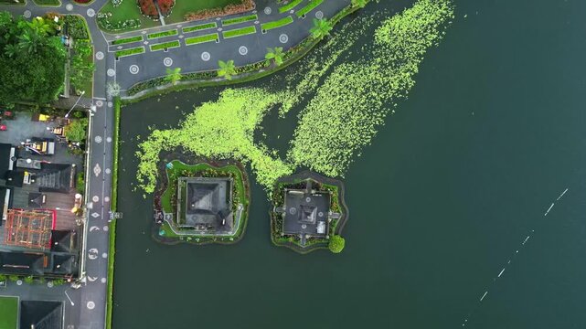 Aerial view of the serene Danau Beratan temple complex surrounded by lush greenery and dark waters, Candikuning, Kabupaten Tabanan, Indonesia.