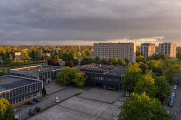 Urban landscape with residential apartment blocks surrounded by green trees during golden hour in Warsaw, Poland. Modern low-rise building with parking lots. Dramatic evening clouds with warm sunlight