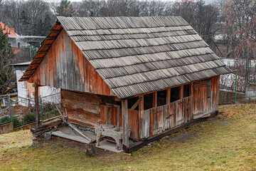 Traditional wooden log cottage with a thatched roof and small windows, surrounded by a woven wooden...