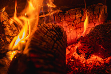 Cozy background of burning logs in a fireplace. Close-up of glowing embers and warm flames. Concept...