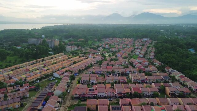 Drone glides above Bancao-Bancao&rsquo;s pastel-roof suburb in Puerto-Princesa, drawing from regimented rows of townhouses across lush forest toward a tranquil bay backed by misty mountain ridges.