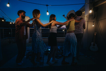 Friends celebrating together on an illuminated outdoor rooftop, dancing and having a festive time...