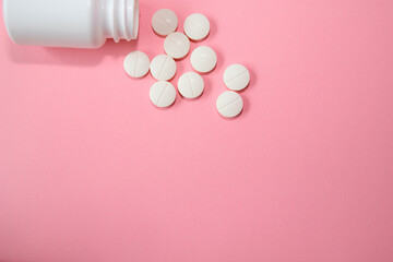 White pills are scattered on a pink background next to an open bottle, showcasing a pharmaceutical product in a clean and vibrant setting for health and wellness concepts