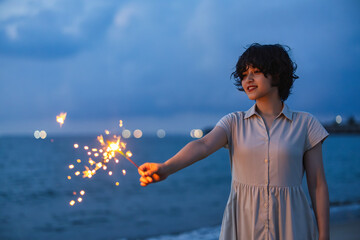 夕暮れの海辺で花火を楽しむ女性モデルの柔らかなボケ感を活かしたポートレート