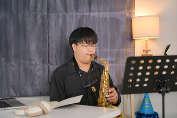 Young Asian man playing saxophone indoors in a cozy room with soft lighting