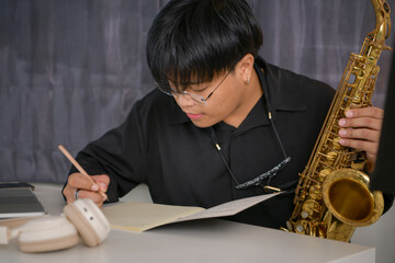 Young Asian man playing saxophone indoors in a cozy room with soft lighting