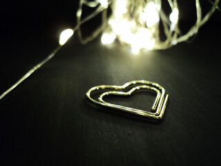 Close-up of a metallic heart-shaped bookmark on a black background with soft yellow fairy lights....