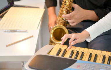Two young Asian man and woman performing music indoors with keyboard and saxophone