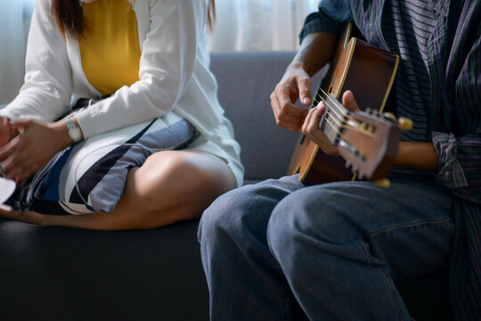 Happy Asian woman enjoying music with headphones while man plays guitar and harmonica