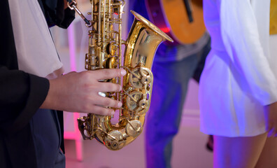 Young Asian band performing music indoors with guitar, keyboard, saxophone, and vocals