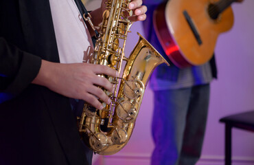 Young Asian band performing music indoors with guitar, keyboard, saxophone, and vocals