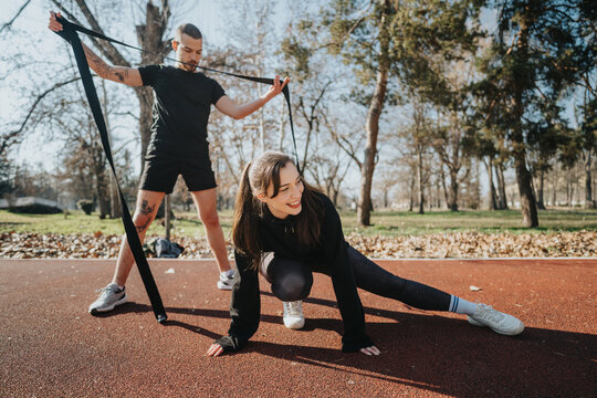 Two teenagers participate in a dynamic outdoor fitness activity, using a resistance band for stretching exercises.