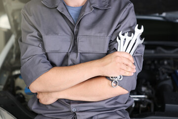 Auto parts. Professional mechanic with different wrenches near open hood of car indoors, closeup