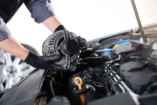 Auto part. Professional mechanic with alternator near open hood of car indoors, closeup