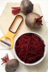 Raw beetroot noodles, fresh vegetables and peeler on white wooden table, flat lay