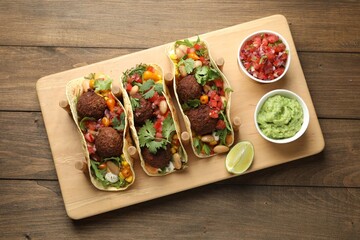 Tasty vegetarian tacos with falafel served with salsa and guacamole on wooden table, top view
