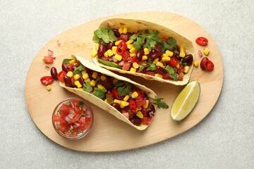 Tasty vegetarian tacos with beans, vegetables and lime on light grey table, top view