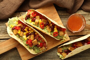 Tasty vegetarian tacos served with sauce on wooden table, flat lay
