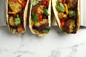 Tasty vegetarian tacos with falafel, tofu, beans and vegetables on white marble table, top view....