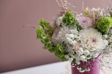 Beautiful flowers in vase on white table against pink background, closeup. Space for text