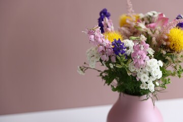 Beautiful flowers in vase on white table against pink background, closeup. Space for text