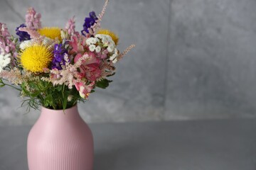 Beautiful flowers in vase on grey table, closeup. Space for text
