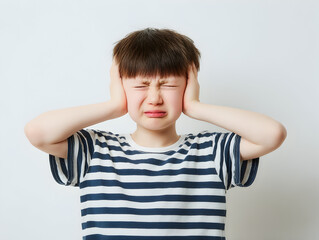 Little boy blocking his ears and wincing in discomfort on a plain backdrop providing room for headlines about noise pollution classroom management and listening skills