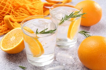 Sparkling water with orange slices and rosemary on grey table, closeup