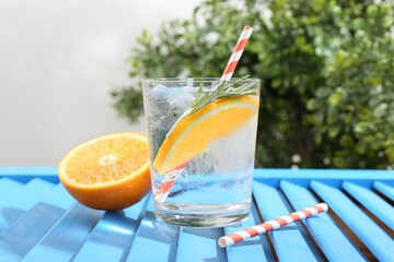 Refreshing soda water with orange slice and rosemary in glass on light blue wooden table, closeup