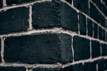 A dark brick wall corner with white mortar, creating a textured backdrop. Close-up shot of textured...