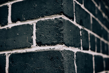A dark brick wall corner with white mortar, creating a textured backdrop. Close-up shot of textured...