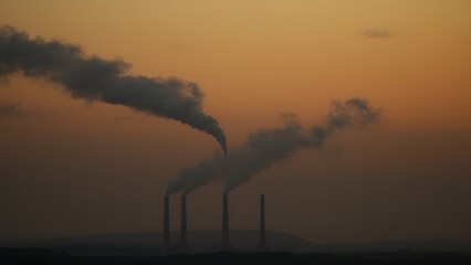 Obraz premium Industrial smokestacks releasing dense smoke at dusk, creating a hazy atmospheric landscape with muted colors.