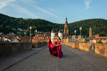 schöne Frau in rotem Kleid, tanzt in Heidelberg in der Morgensonne, über die alte Brücke.