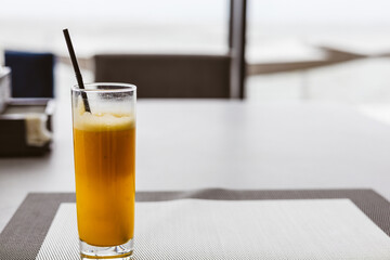 A glass of fresh orange juice with a black straw on a table in a cafe or restaurant. A tall glass of fresh orange juice sits on a table with a placemat. The background is blurred A drink for breakfast