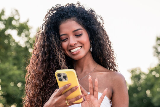 Smiling young woman using smartphone outdoors in park - Powered by Adobe