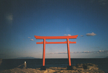 Red torii gate standing on rocky coastline overlooking calm ocean in japan